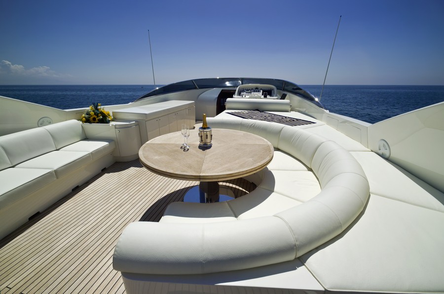 Top deck of a superyacht with white seating and a bottle of champagne on a table. In the distance is the ocean and blue sky.