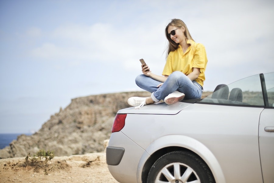 Woman sitting on top of car trunk checking the Control4 app on her smartphone. 