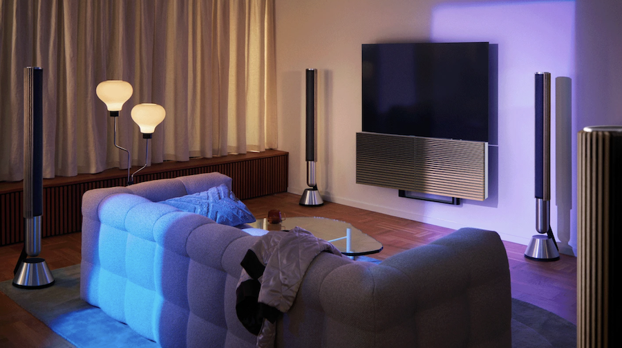 A living room lit by warm and purple lighting with a B&O sound system arranged around the TV. 