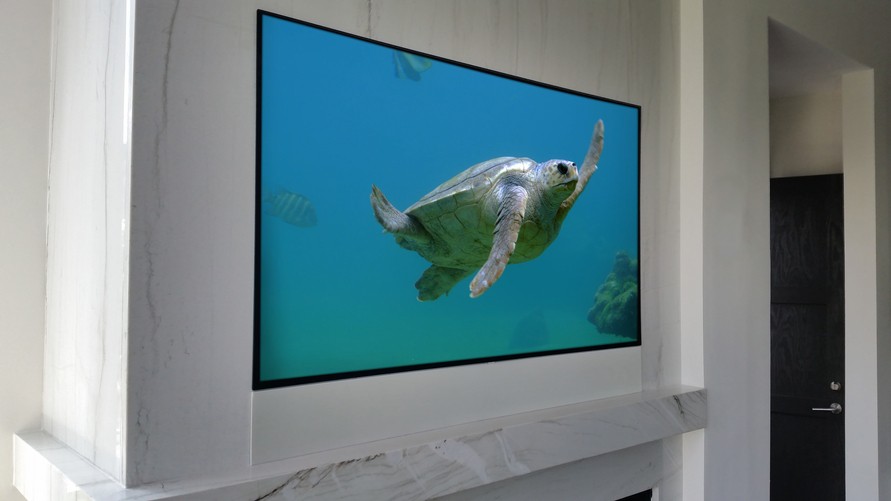 A flatscreen TV with a white hidden sound bar installed within the wall below it. 