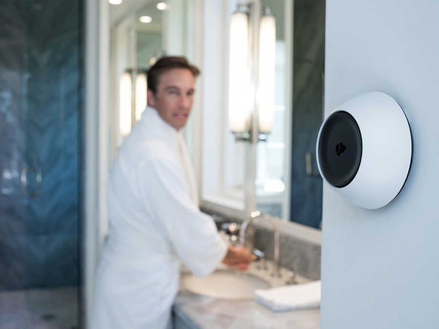 A man in a bathrobe speaks to his Josh.ai voice control device mounted on the wall. 