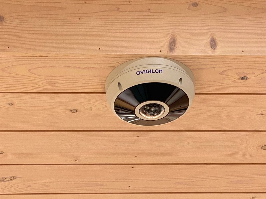 An Avigilon home surveillance camera on a wooden ceiling. 