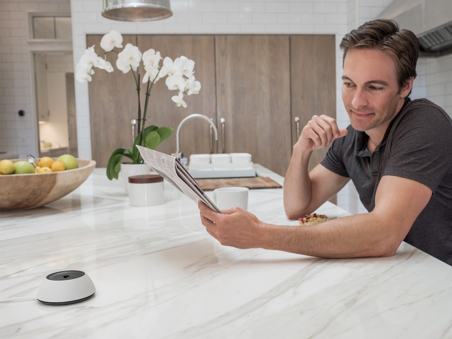 Man leaning on kitchen counter next to a Josh.ai voice controller.  