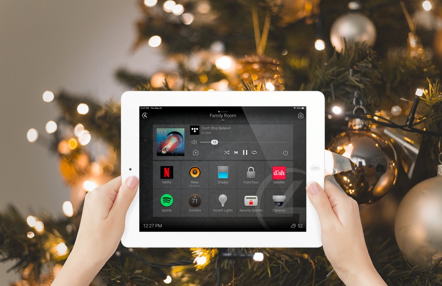 Two hands holding a tablet with a Control4 smart home interface. In the background is a Christmas tree. 