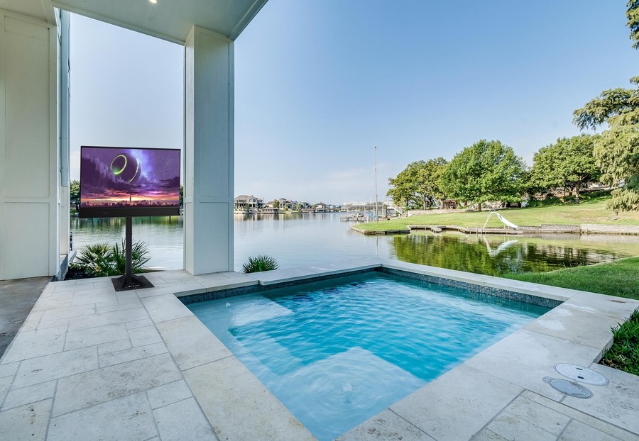 A backyard pool with an outdoor TV mounted on a stand. 