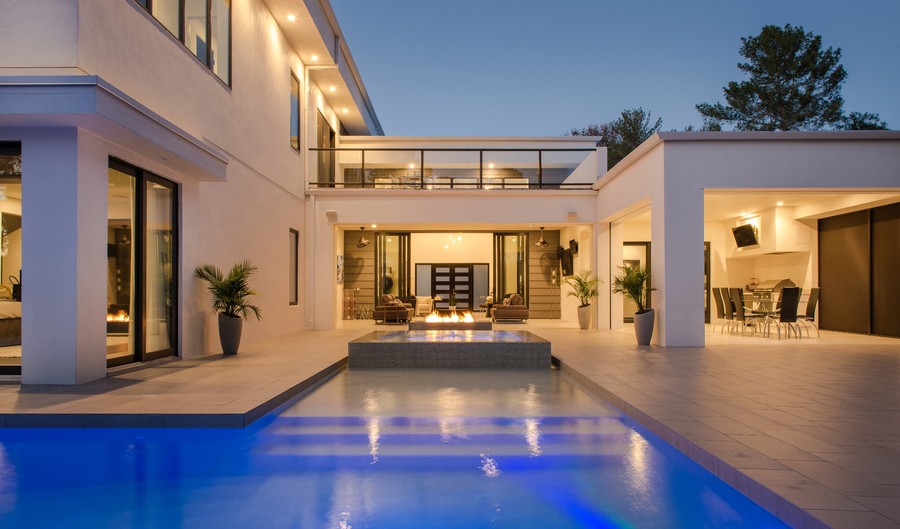 A white modern house with an inground pool and outdoor lighting. 